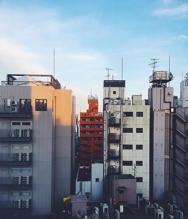 A cityscape featuring various buildings and architectural styles under a bright blue sky, capturing a quiet urban atmosphere.