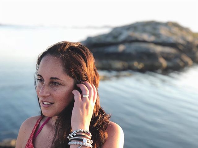A woman looks out at the ocean wearing bracelets and a ring with a rock in the background.