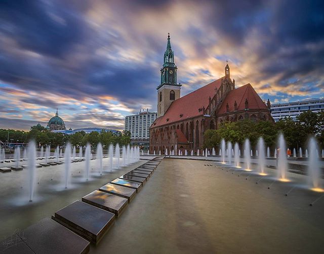 A beautiful view of St. Mary's Church in Berlin, Germany, with fountains in the foreground under a cloudy sky.