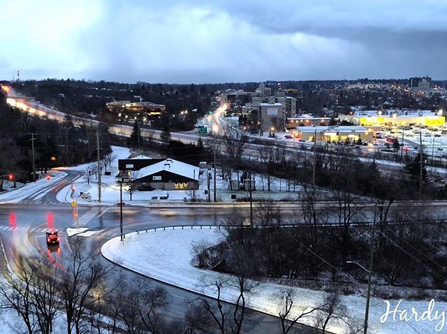 A tranquil winter cityscape shows snow-covered roads and buildings under an overcast sky.