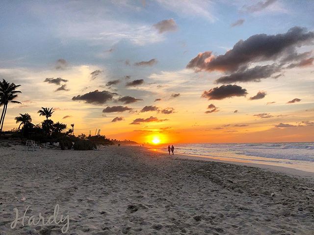 A couple walks on a sandy beach enjoying a peaceful, beautiful sunset over the ocean.