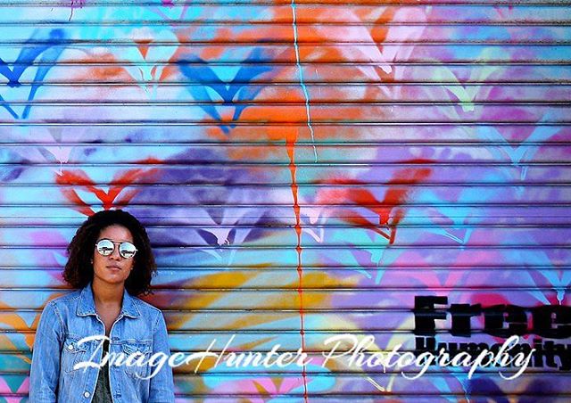 A young woman in sunglasses poses in front of colorful graffiti art. 
