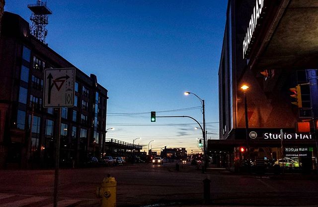 A calm street scene at dusk shows buildings, a yield sign, and a fire hydrant under a blue sky.