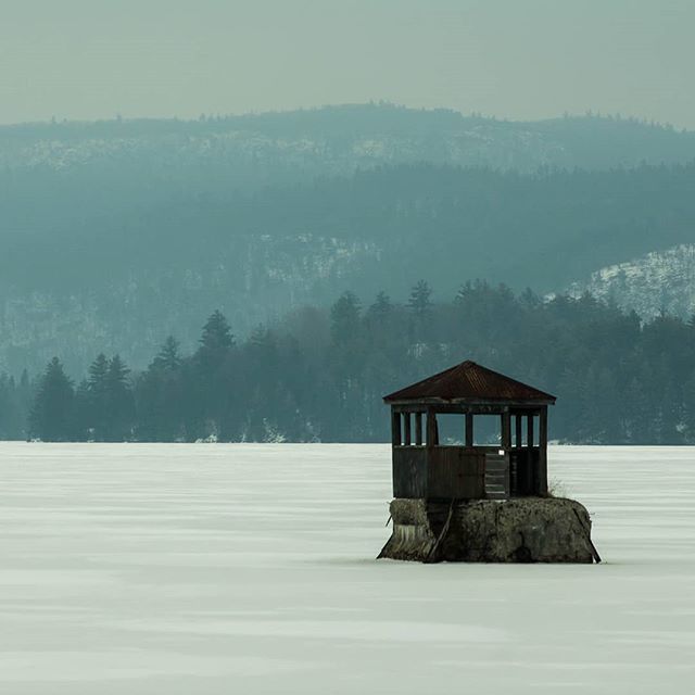 A lone gazebo sits on a rock in a frozen lake, with mountains in the distance.