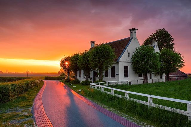 A picturesque rural landscape featuring a house along a road during a vibrant sunset.