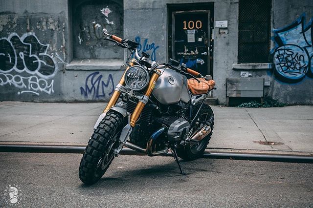 A custom BMW R Nine T motorcycle parked on a city street with graffiti walls, exuding vintage style and urban energy.