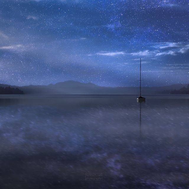 A lone sailboat sits on a calm lake under a starry night sky, creating a sense of peace and wonder.