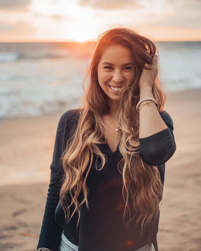 A smiling woman enjoys the sunset at the beach, feeling happy and relaxed by the ocean.