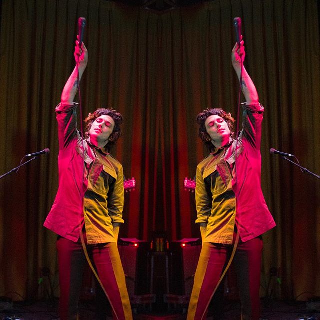 A singer energetically performs on stage, holding a microphone against a backdrop of warm, vibrant lighting.