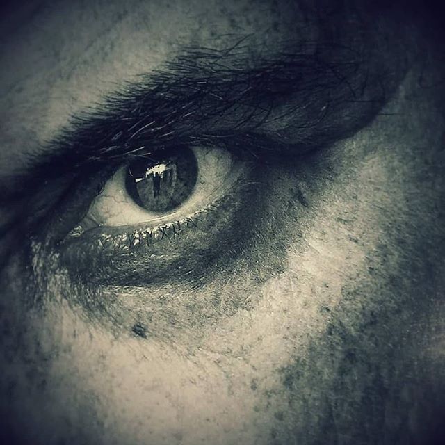 A black and white close-up of a man's eye with a reflected figure, conveying intensity and emotion.