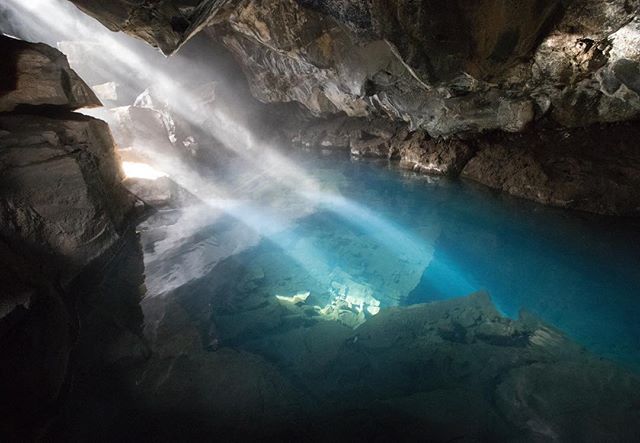 Sunbeams illuminate a clear blue pool inside a dark cave, creating a tranquil and mysterious scene.