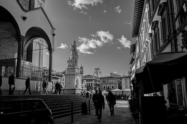 A black and white photo of people walking in a city square with a statue in the background.