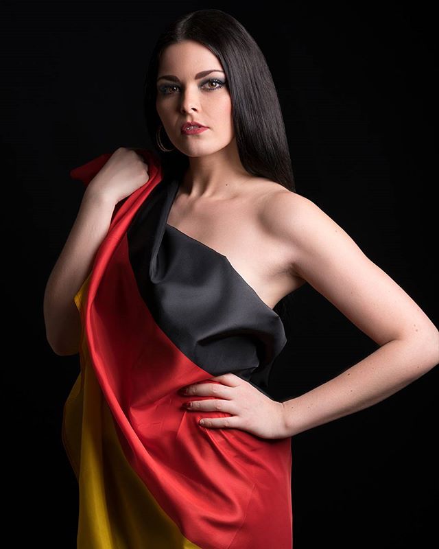 A woman draped in the German flag poses in a studio setting against a black backdrop.