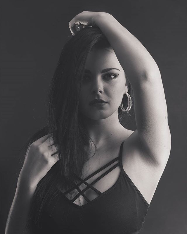 Portrait of a brunette woman in a black top with hoop earrings posing in a studio.