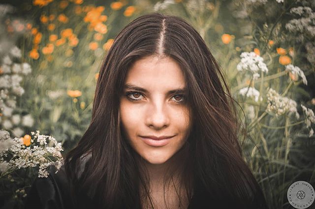 Portrait of a young woman with brown hair in a field of flowers, exuding calm and natural beauty.