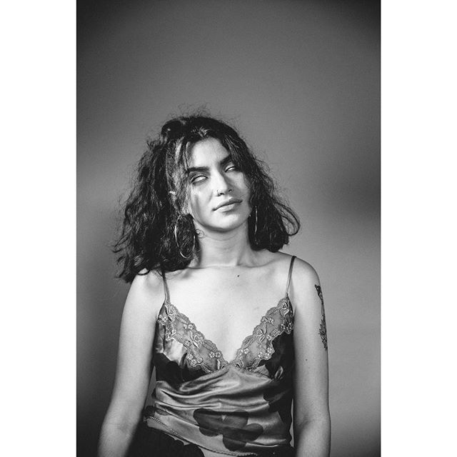 A black and white portrait of a woman with hoop earrings and a camisole in a studio setting.