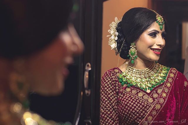 A smiling bride wearing traditional Indian jewelry and a red dress on her wedding day.