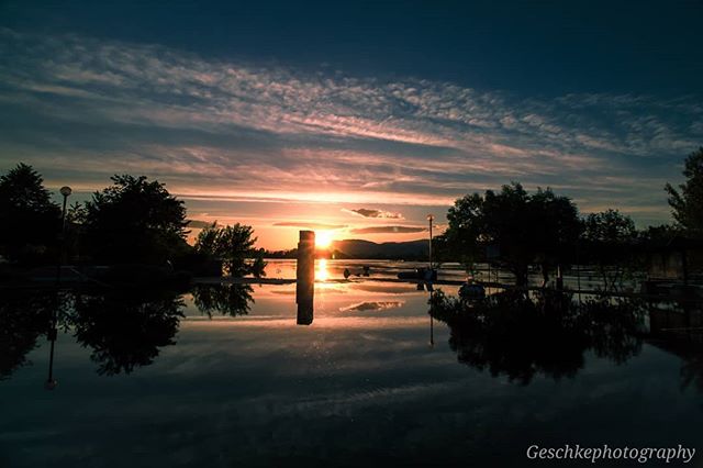 A tranquil sunset reflecting off water with silhouettes of trees against a colorful sky.