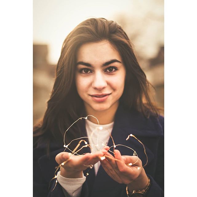 A beautiful woman holds glowing fairy lights in her hands, casting a warm and dreamy ambiance.