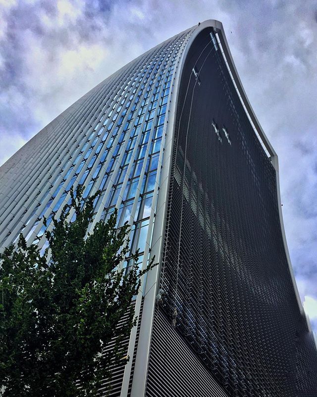 A modern skyscraper rises dramatically against a cloudy sky, showcasing innovative architecture in an urban setting.