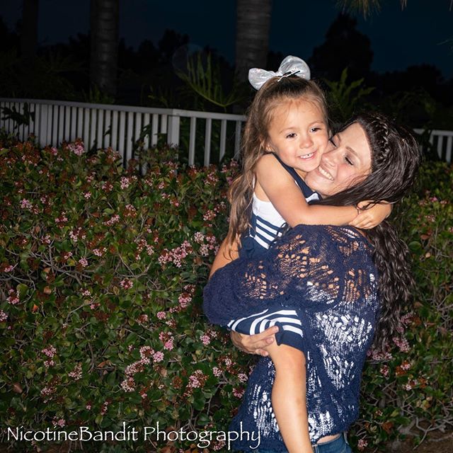 A mother holds her young daughter in a loving embrace in a garden setting at night.