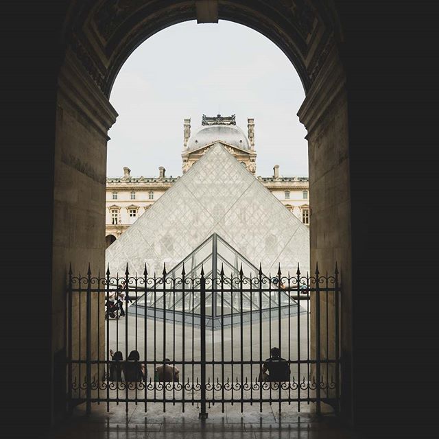 The Louvre Pyramid is viewed through an archway and gate, capturing a serene moment in the heart of Paris.