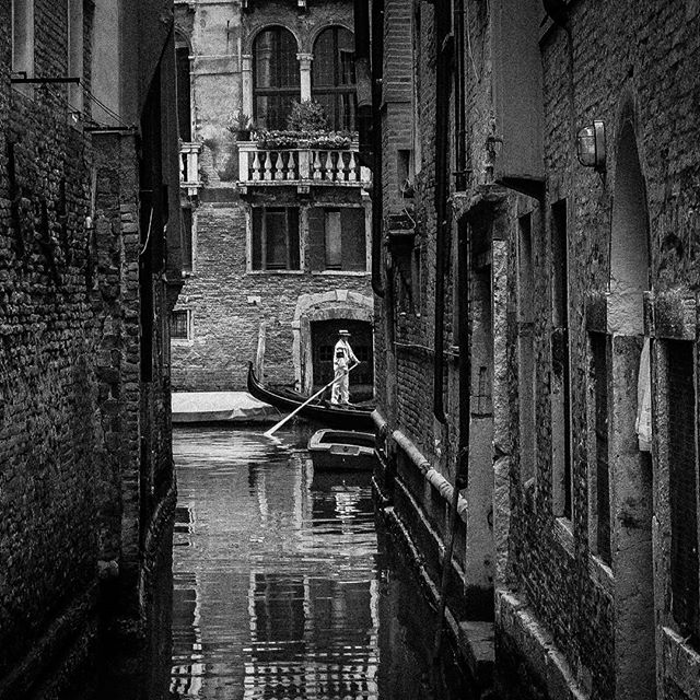 A gondolier navigates a gondola through a narrow canal in Venice, Italy, surrounded by historic buildings.