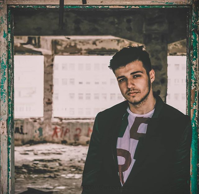 A man poses inside an abandoned building with graffiti and crumbling walls, creating an urban and serious atmosphere.