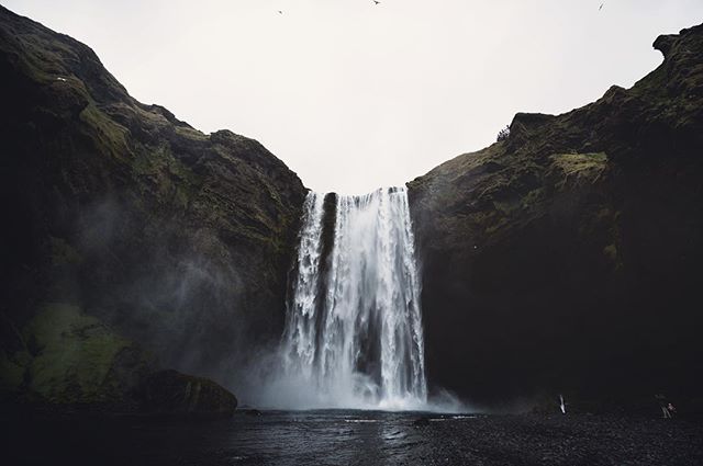 A majestic waterfall cascades between dark cliffs in Iceland, shrouded in mist. Scenic landscape.
