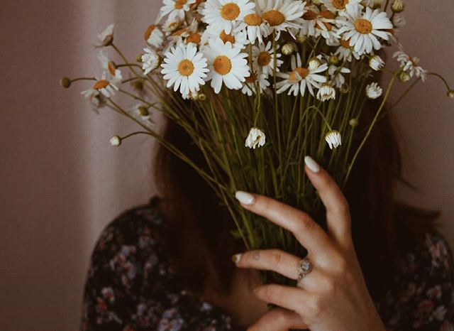 A woman hides her face behind a bouquet of white daisies, creating a soft and intimate portrait.