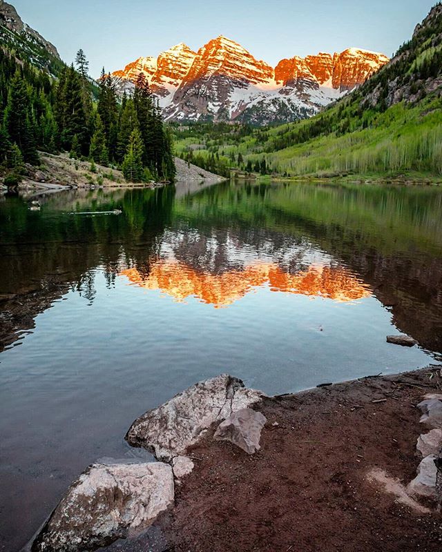 Scenic mountain peaks are reflected in a calm lake surrounded by lush green trees.