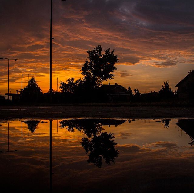 Dramatic sunset reflects in a puddle, silhouetting the cityscape for a tranquil and mysterious scene.