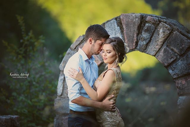 A loving couple embraces in front of a stone archway, bathed in soft, natural light.