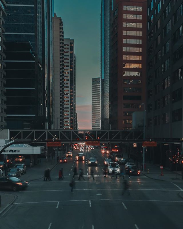 City street with pedestrians and cars among tall buildings at dusk.