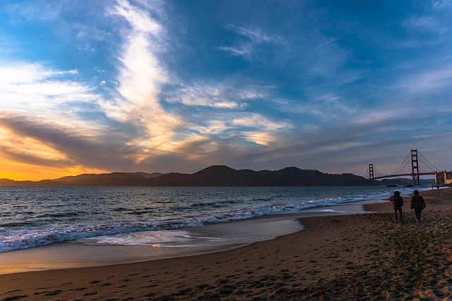 Scenic view of the Golden Gate Bridge at sunset with people walking on the beach, perfect for travel and tourism campaigns.