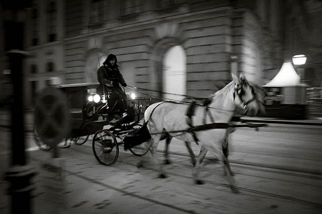 A horse-drawn carriage moves through the city at night in a vintage black and white style.
