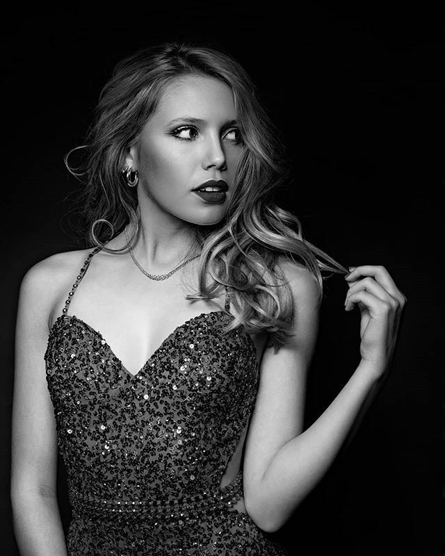 Elegant woman poses in a sequined dress with jewelry against a black backdrop, evoking confidence and sophistication.