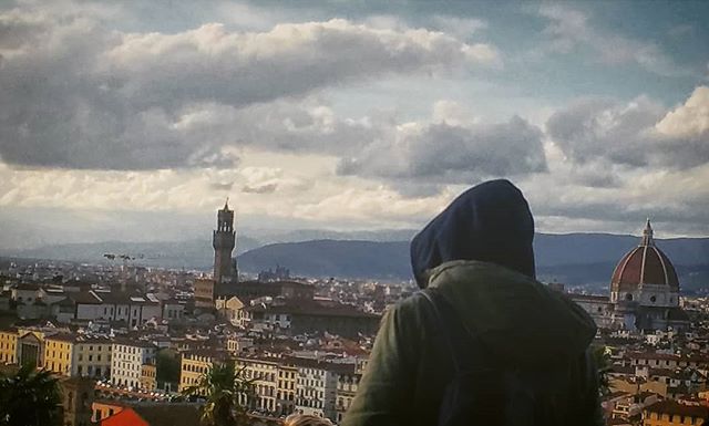 A person with a hoodie looks over the cityscape of Florence, Italy, on a cloudy day.
