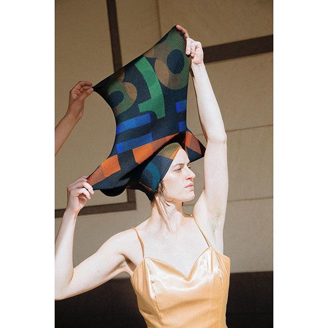 A confident woman in a yellow dress poses with a colorful headscarf indoors.