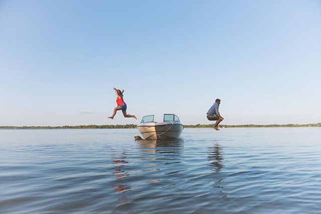 A woman and a man are jumping into a lake from a boat on a sunny day.