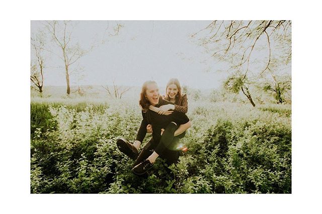 A happy couple enjoys a piggyback ride in a sunny field, surrounded by lush greenery.