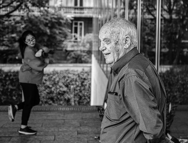 A candid street scene featuring an elderly man and a young woman in an urban setting.