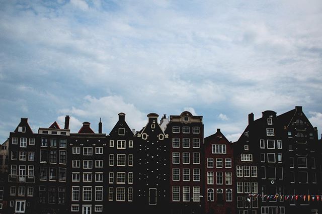 A row of historic buildings in Amsterdam under a cloudy sky, showcasing classic urban architecture and tourism appeal.