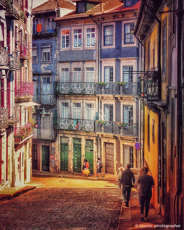 A colorful street scene in Porto, Portugal, featuring historic buildings and people walking along the cobblestone street.