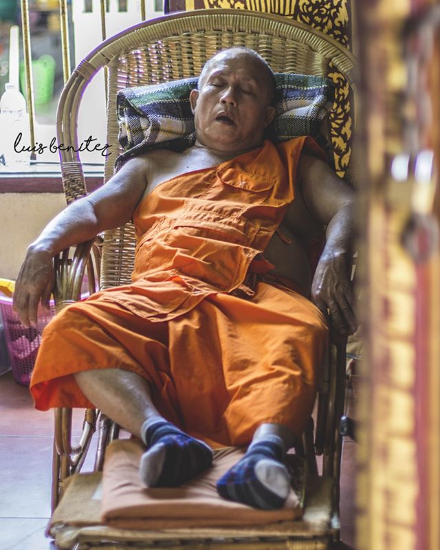 A monk in orange robes rests peacefully in a woven chair, capturing a moment of serene tranquility.