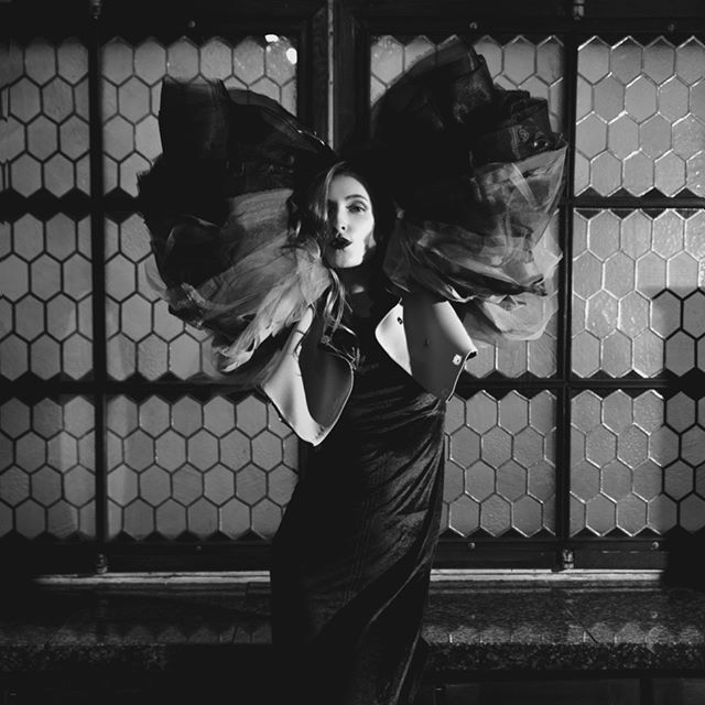 A woman poses dramatically in a high-fashion, black and white studio portrait with a large, sculptural garment.