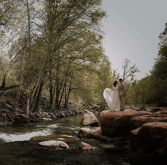 A bride and groom pose on rocks by a river in a romantic outdoor wedding photo.