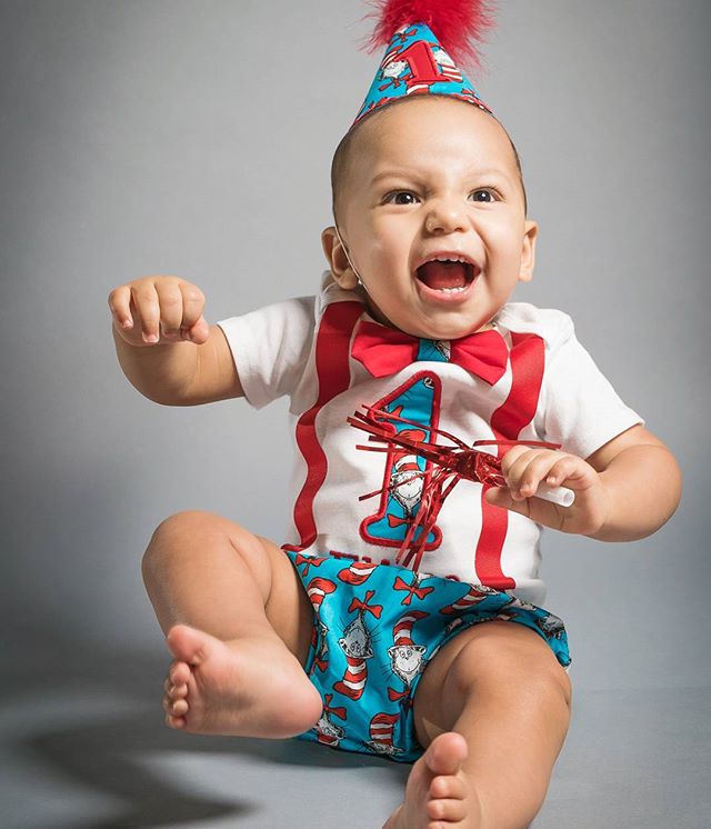 A cheerful baby celebrates their first birthday in a party hat, bowtie, and suspenders, capturing a moment of joy and energy.