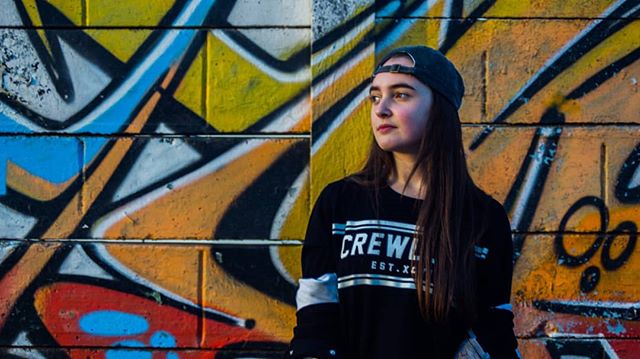 A young woman poses against a graffiti wall in an urban setting.