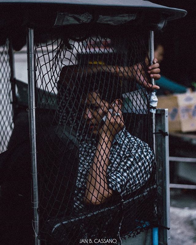 A man sits in a netted vehicle, creating a thoughtful and intimate street portrait.